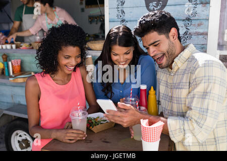 Smiling friends using mobile phone at food truck van Stock Photo