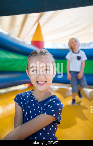 Portrait of girl sitting on bouncy castle while brother playing in background Stock Photo