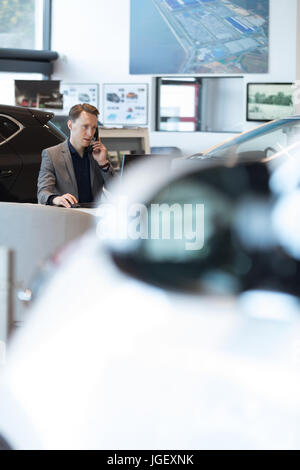 Car salesperson talking on landline phone in car showroom Stock Photo