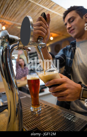 Young bartender pouring drink from tap in glass at restaurant Stock Photo