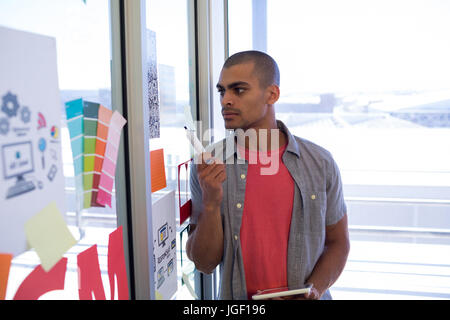 Male executive reading sticky notes on glass door in office Stock Photo