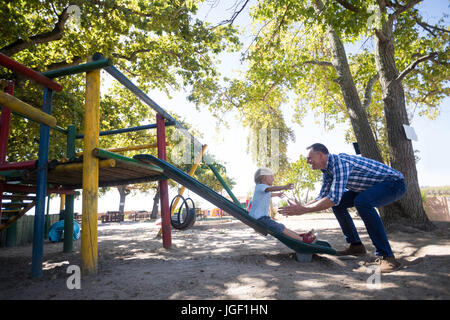 Side view of father looking at son sliding at playground Stock Photo