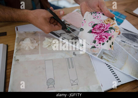 Cropped hands of designer cutting papers at table in studio Stock Photo