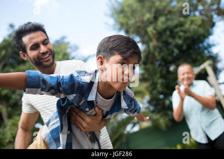 Grandfather looking at man playing with son while standing at park Stock Photo