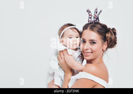 Mom and daughter in white clothes embrace. The girl in the crown, the princess Stock Photo