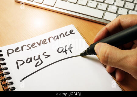 Hand is writing perseverance pays off on a note. Stock Photo