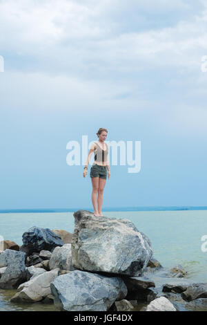 Girl practicing yoga on the rocks against the blue sky and the azure sea. Relaxation and Stretching. Young slim sporty woman do yoga outdoors. Stock Photo