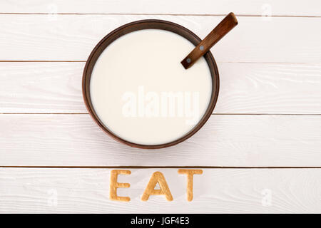 Close-up view of milk and spoon in bowl and word eat from breakfast cereal letters on wooden table top Stock Photo