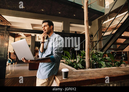Shot of young business man thinking with laptop during break. Businessman in modern office using laptop. Stock Photo