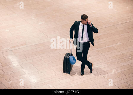 Top view shot of young businessman standing at airport terminal with suitcase and talking on phone. Business traveler making a phone call while waitin Stock Photo