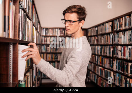 Young university student taking a book from shelf in library. College student picking a book from bookshelf in library. Stock Photo