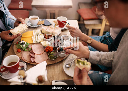 Close up of young people sitting around cafe table and eating with focus on hands and food. Group of students having food in college canteen. Stock Photo