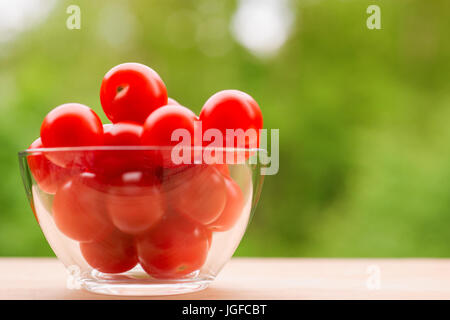 Red cherry tomatoes in glass on wooden table. Selective focus. Against green natural defocused background Stock Photo