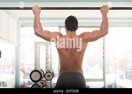 Handsome shirtless man doing pull ups in the L-sit position on horizontal  bar outdoors at night. Calisthenics training. Stock Photo