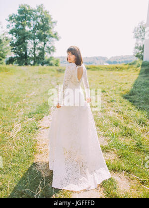 The lovely photo of the smiling bride in the long wedding dress. Back view. Stock Photo