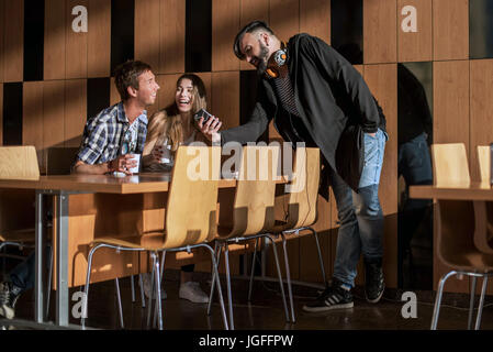 Group of friends relaxing in common room. Boy showing something on his phone to his friends. Stock Photo