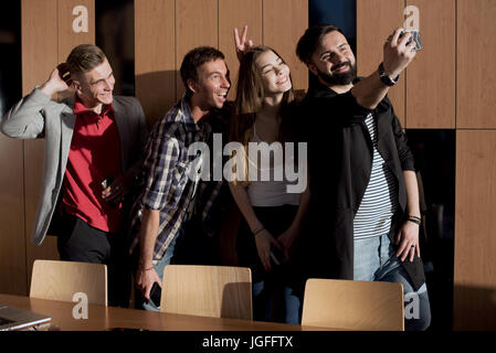Four young people standing in the room by the window and making selfie. Stock Photo