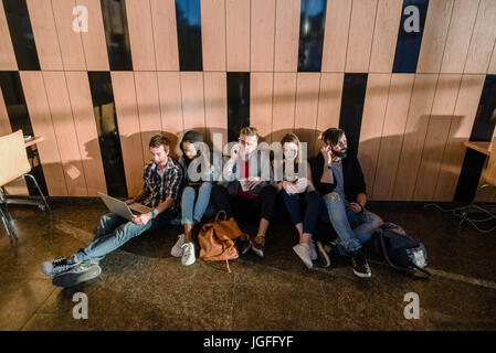 Group of students relaxing in the big room. Students sitting on the floor. Stock Photo
