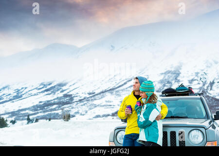 Caucasian couple hugging and leaning on car in winter Stock Photo