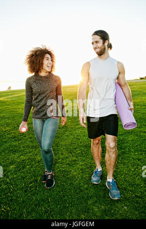 Couple walking in sunny field carrying exercise mat Stock Photo