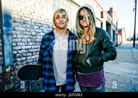 Caucasian couple with skateboard posing on urban sidewalk Stock Photo