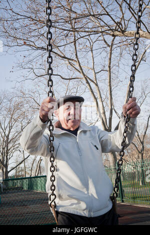 Carefree Hispanic man on swing in park Stock Photo