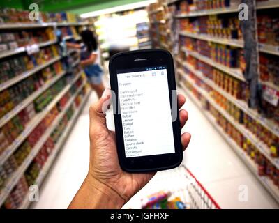 Photo of a hand holding a smartphone with a grocery list while inside a grocery store Stock Photo