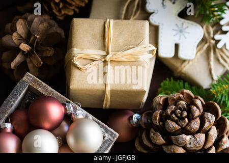 Christmas and New Year gift boxes wrapped in craft paper, twine bow, pine cones, fir tree branches, ornaments, baubles in wood box, cozy festive atmos Stock Photo