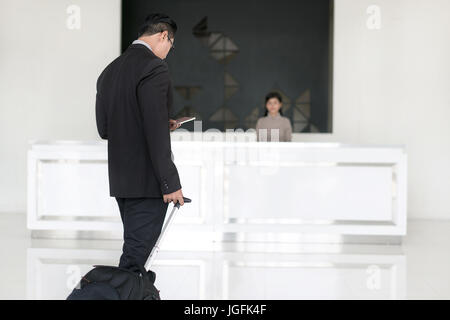 Asian businessman walking to check in at hotel reception front desk. Stock Photo