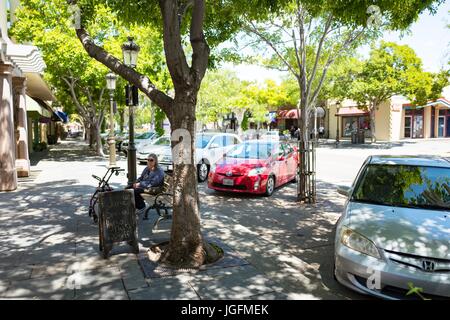 A woman sits on a bench near parked cars, on First Street in downtown Livermore, California, June 12, 2017. Stock Photo