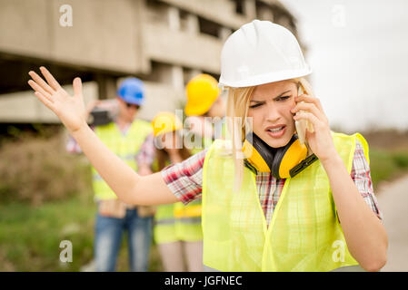 Beautiful young female construction architects using phone in front building damaged in the disaster. Stock Photo