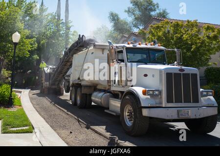 Pulverized asphalt pours from a conveyor into a dump truck, releasing a cloud of dust, during a road construction and resurfacing project in the San Francisco Bay Area suburb of San Ramon, California, June 26, 2017. Stock Photo