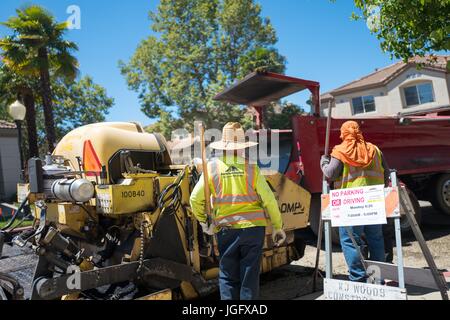 Construction workers for American Asphalt work to lay a new road surface, wearing wide brimmed hats and turbans to protect themselves from the bright sun, during a road construction and resurfacing project in the San Francisco Bay Area suburb of San Ramon, California, June 26, 2017. Stock Photo