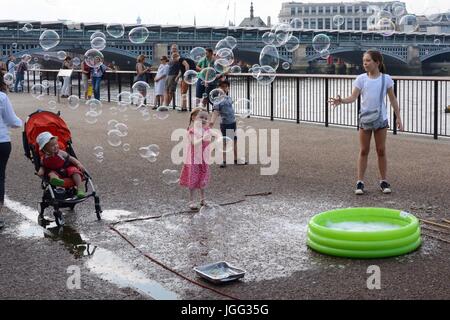 London, UK. 6th July 2017. A busker entertains the crowd with his giant bubble maker on the South Bank in London. Credit: Patricia Phillips/Alamy live news Stock Photo