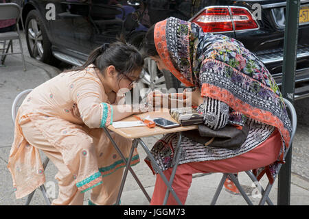 An Islamic woman in traditional clothing decorates a young girl's hand with henna to celebrate Eid Al Fitr holiday marking the end on Ramadan. Stock Photo