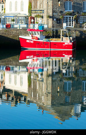 A hot and tranquil summers morning at the picturesque fishing village of Padsow in Cornwall, England with bright red fishing boat against harbour wall Stock Photo