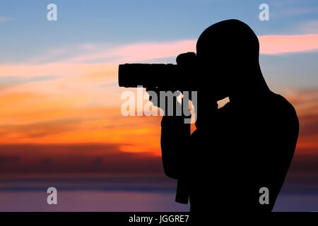 Photographer taking pictures, silhouette of a man with camera over beautiful orange sunset background, photographing amazing view of a nature near the Stock Photo