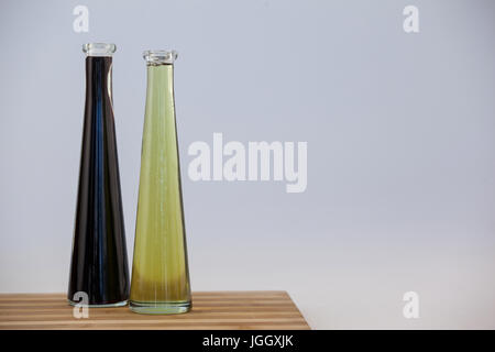 Black and green olive oil in bottle on table against wall Stock Photo