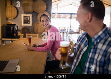 Friends interacting with each other while having glass of beer in bar Stock Photo