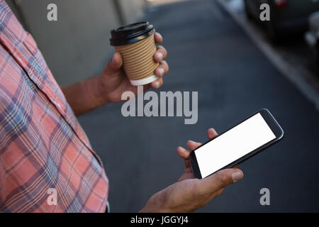 Midsection of man having coffee while using mobile phone Stock Photo