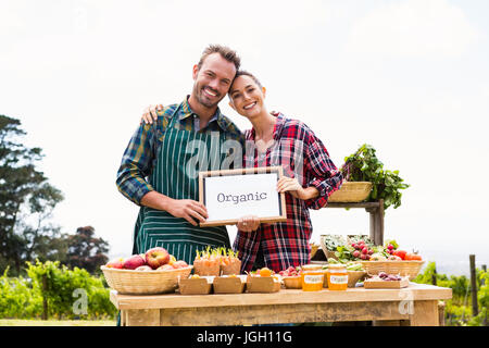 Portrait of smiling couple with blank blackboard selling vegetables at farm Stock Photo