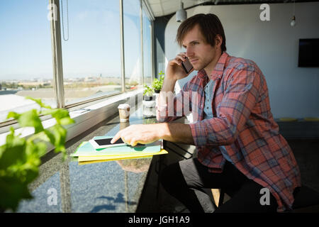 Businessman talking on phone while using digital tablet by window at office Stock Photo