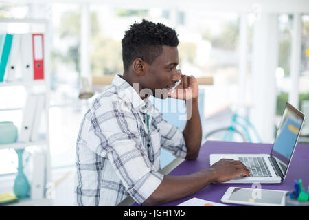 Smiling executive talking on mobile phone while using laptop in office Stock Photo