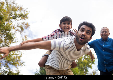 Smiling grandfather looking at man giving piggy backing to son with arms oustretched in yard Stock Photo