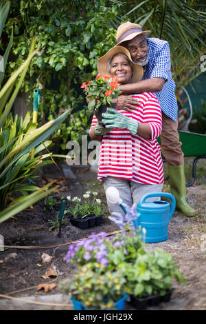 Man embracing woman kneeling on field during gardening in yard Stock Photo