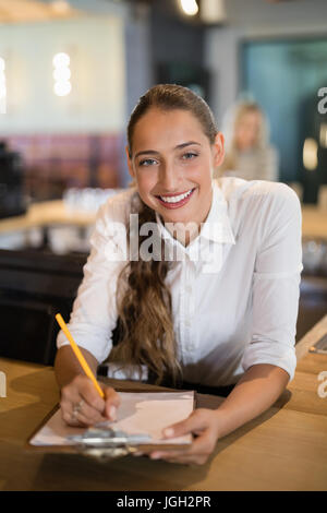 Portrait of smiling bartender writing on clipboard at bar counter Stock Photo