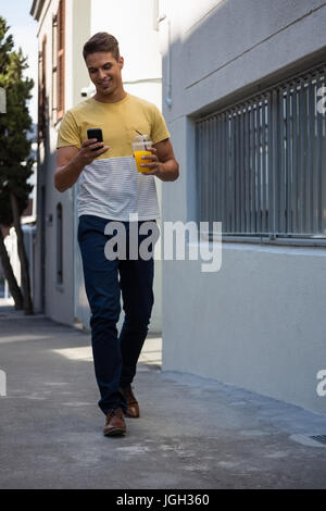 Full length of young man having juice while using mobile phone by wall Stock Photo