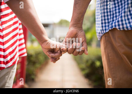 Cropped image of senior couple holding little fingers while standing in yard Stock Photo
