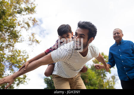 Happy grandfather looking at man giving piggy backing to son with arms oustretched in yard Stock Photo