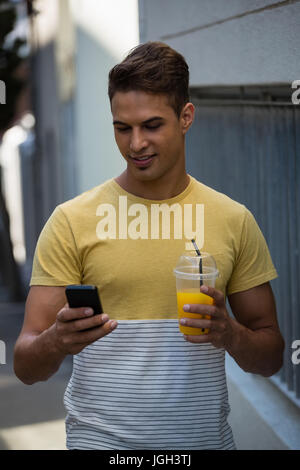 Smiling young man having juice while using mobile phone by wall Stock Photo